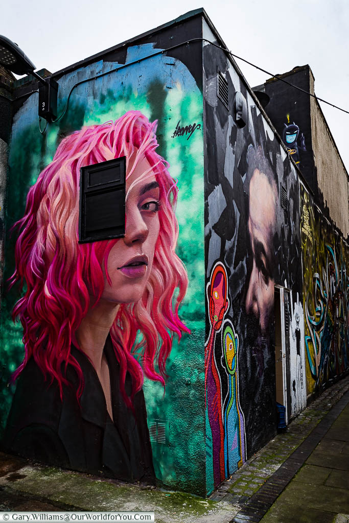A near photo quality mural of a young woman with red & purple hair on the end of a building in Hawley Mews, Camden.