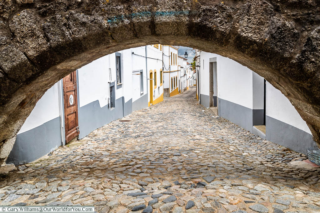 Peering through one of the arches of the Agua de Prata aqueduct to a cobbled white-washed lane of Évora.