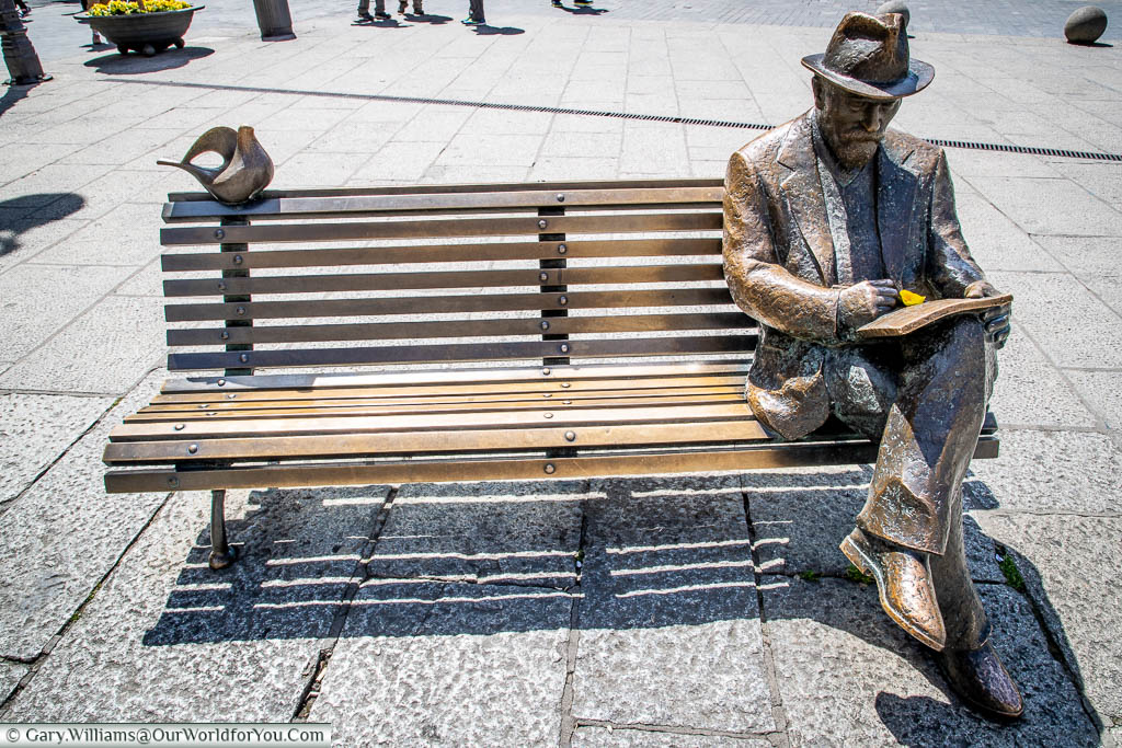 A bronze statue of Antonio Gaudi, seated on a bench, in front of a building he designed, in Leon, Spain.