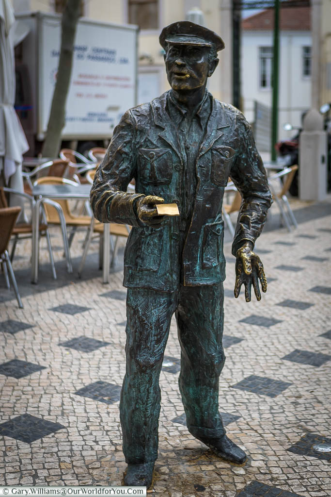 A bronze statue to a lottery ticket seller, complete with peaked hat, in a square in Lisbon.  The extended ticket in his hand has been buffed clean by those touching it for luck.
