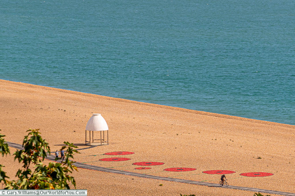 A view from The Leas to the pebble beach below where 6 large red poppies are marked on with painted stones to remember the departure point of soldiers during world war one.