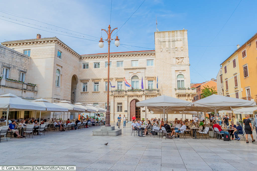 Families sitting at tables under parasols in People’s Square in the old town of Zadar