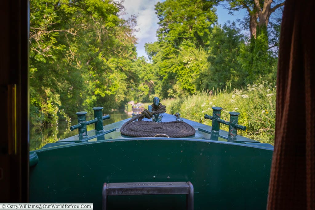 The view from the lounge of the narrowboat, over the bow with its mooring rope neatly placed, along the Kennet & Avon canal