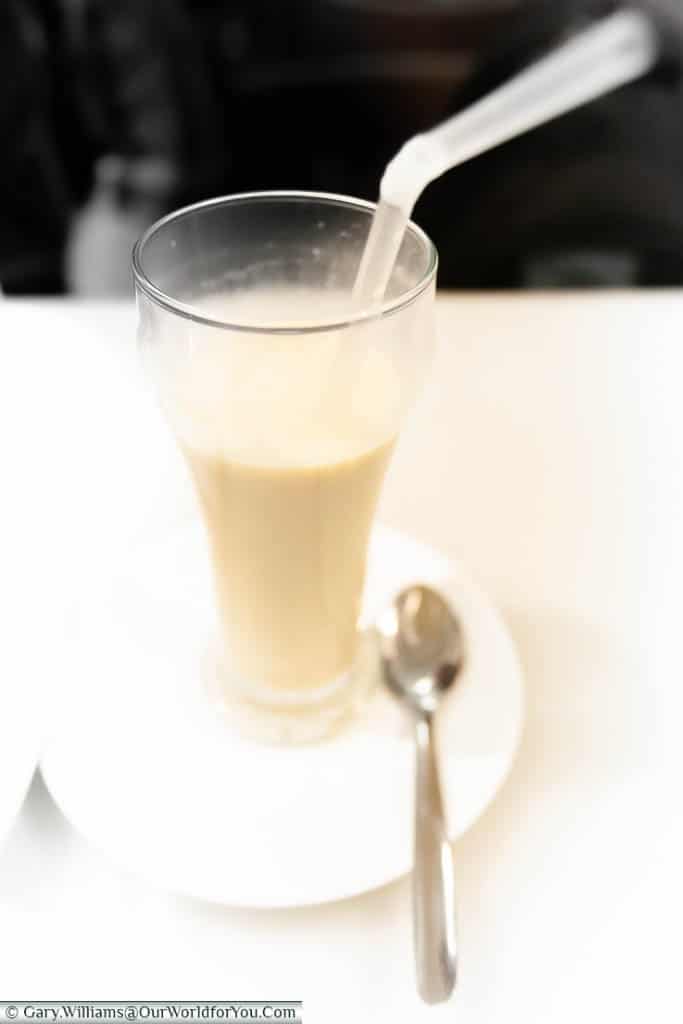 A three-quarters glass of hocata, a creamy, milky, nut based drink with a clear plastic straw.