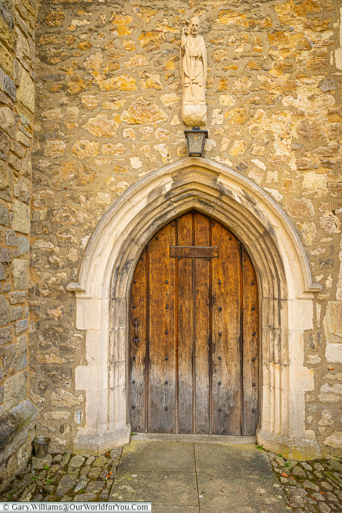 A small statue to Saint Thomas, Archbishop of Canterbury, above a medieval arched wooden doorway in a stone wall in Aylesford Priory