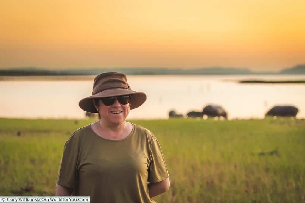 Janis at dusk besides an inlet on Lake Kariba with a herd of hippopotamus grazing at the water's edge