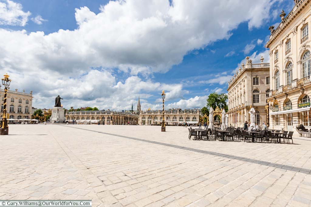 A view from the corner of the Place Stanislas with three storey buildings with cafes at the bottom. You can also see the black and gold wrought iron gates and lamp posts.