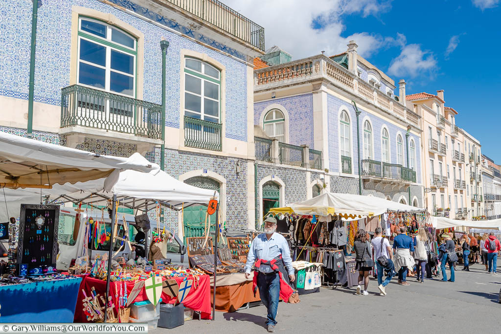 People strolling past market stalls in front of elegant tiled buildings in the Thieves Market, Lisbon, Portugal