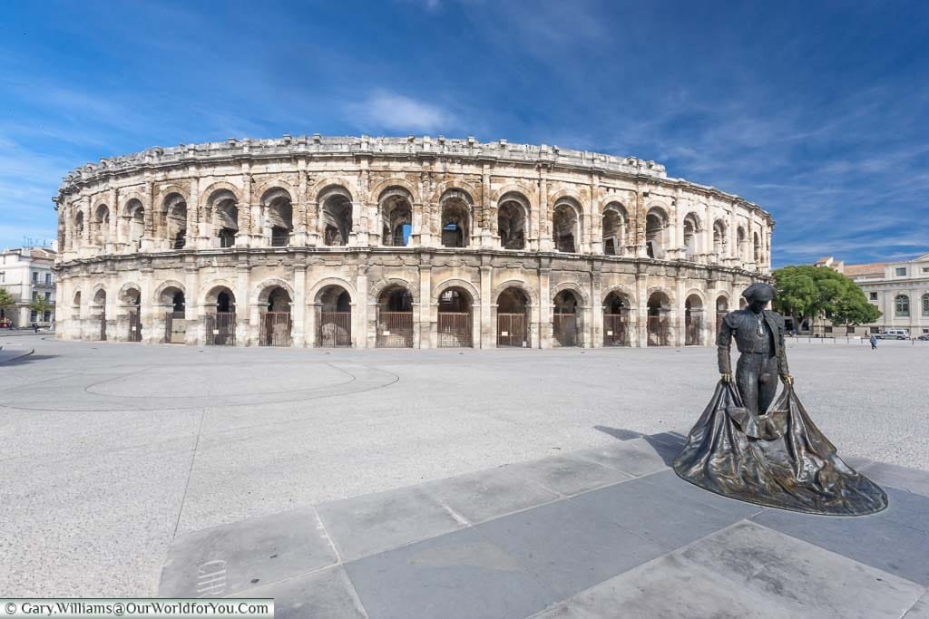 The brass statue of a bullfighter in front of the complete, two-storey, Roman arena in Nîmes.