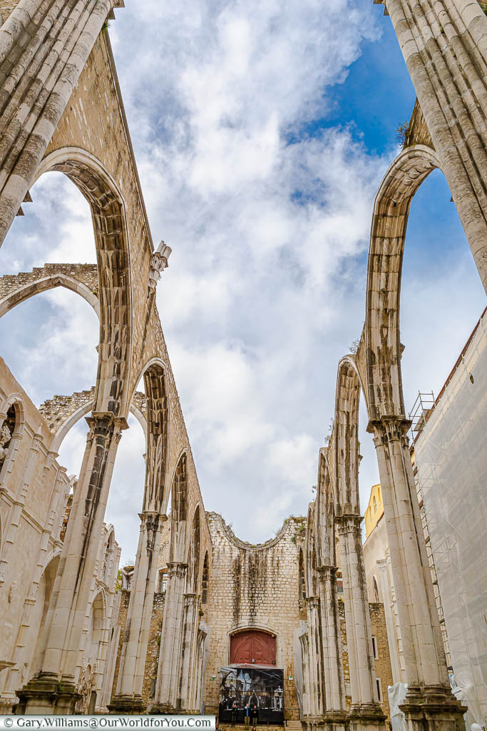 Inside the ruins of the Carmo convent, looking up at the cloudy blue sky over Lisbon, Portugal