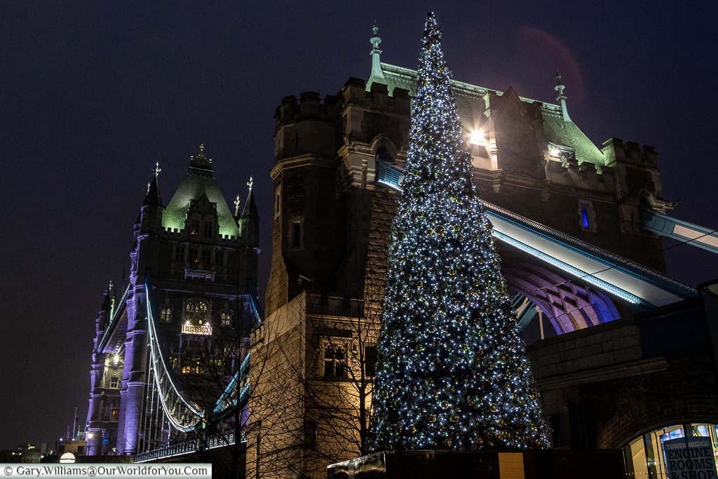 A Christmas tree in front of an illuminated Tower Bridge.