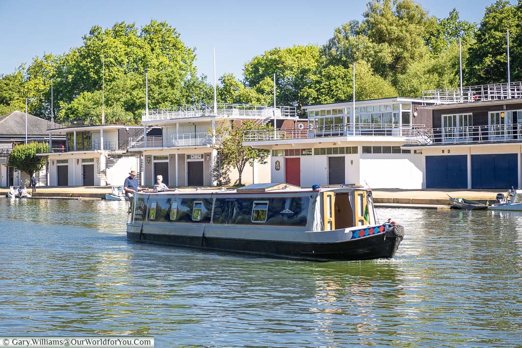 A canal boat passing in front of the different rowing clubs on the banks of the River Thames at Oxford