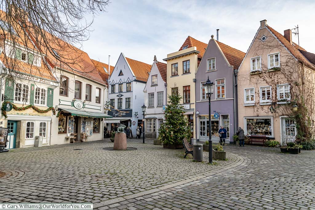 A Christmas tree in a quaint cobbled square, lined with tall thin pastel coloured historic buildings on two sides.