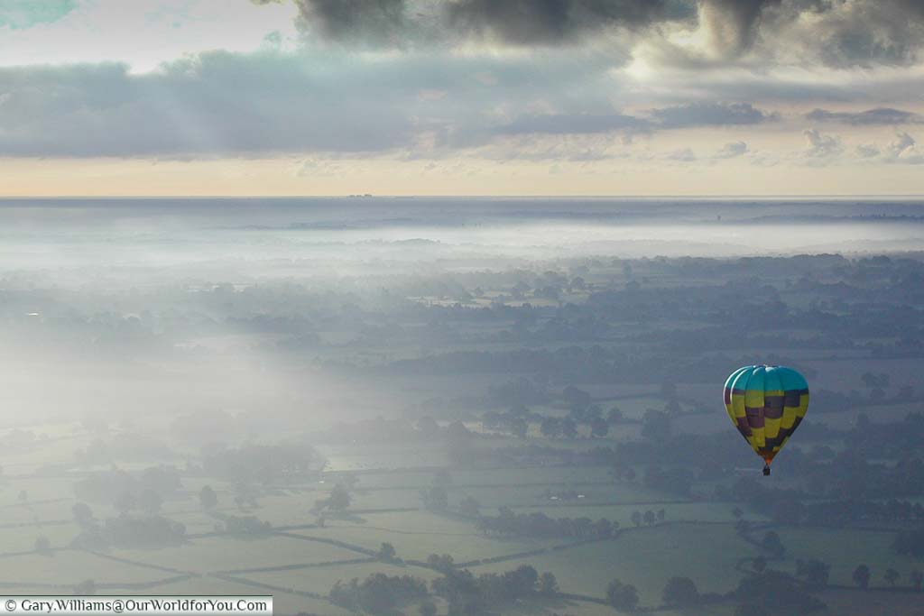 Looking over the Kent countryside on a misty day from a hot air balloon with another balloon in shot.