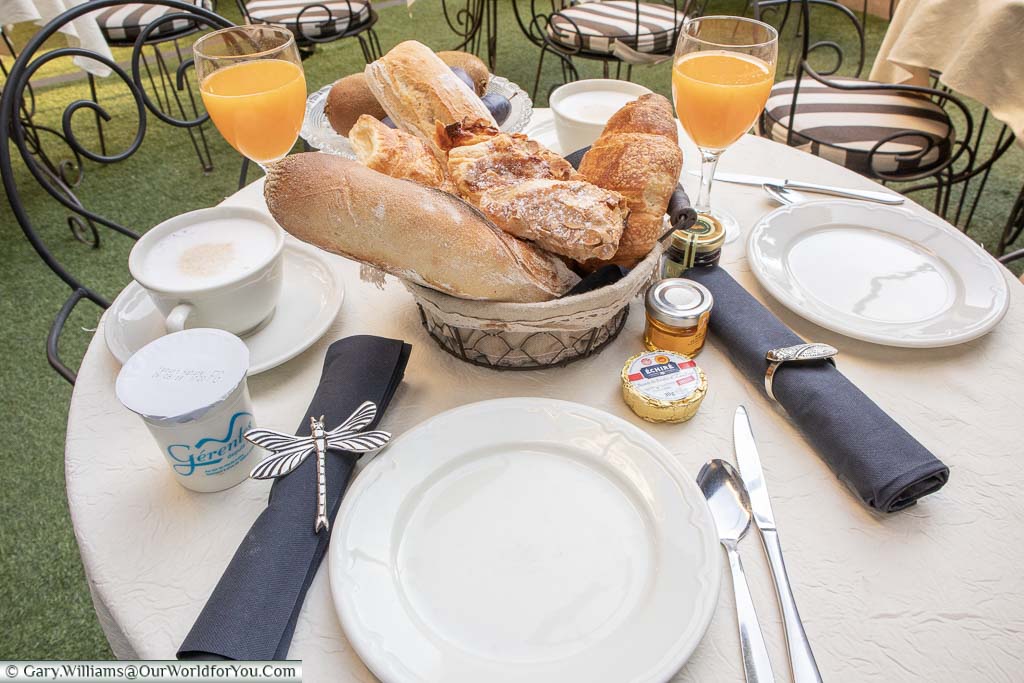 Breakfast at our table in Hotel Gounod, St Remy-de-Provence. A selection of breads and pastries with a fresh orange juice find a cup of coffee.