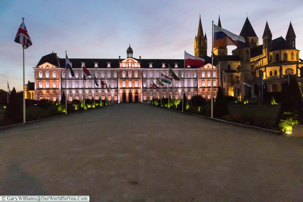 An illuminated Caen town hall alongside L'Abbaye-aux-Hommes under a pale blue and purple sky at dusk.