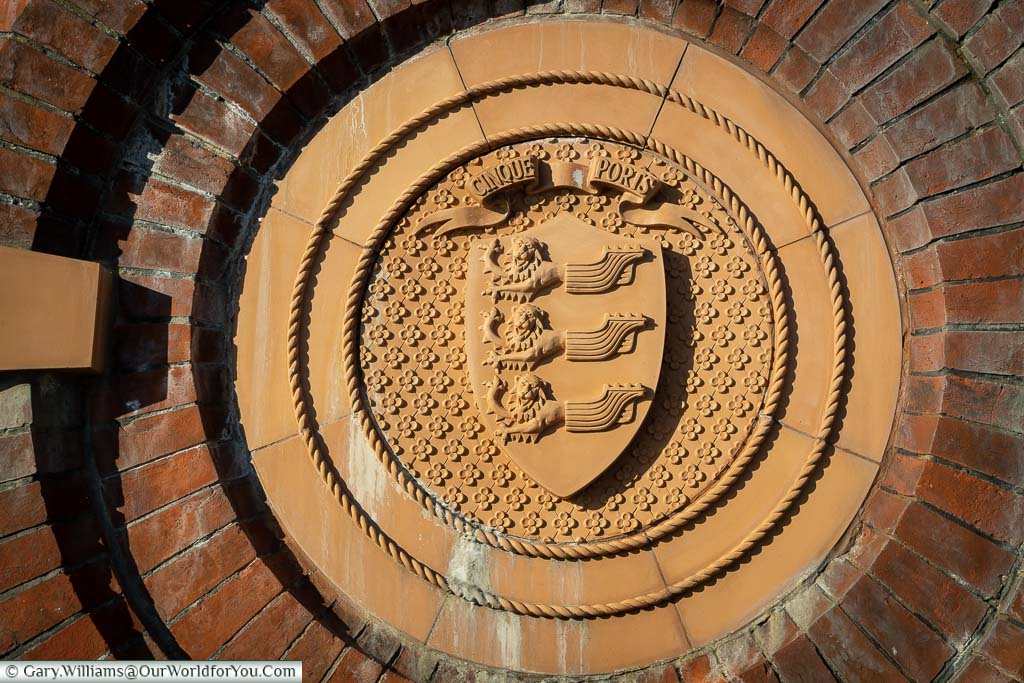 A circular terracotta plaque with the insignia of the cinque ports which is half lion and half ship replicated 3 times on a shield.