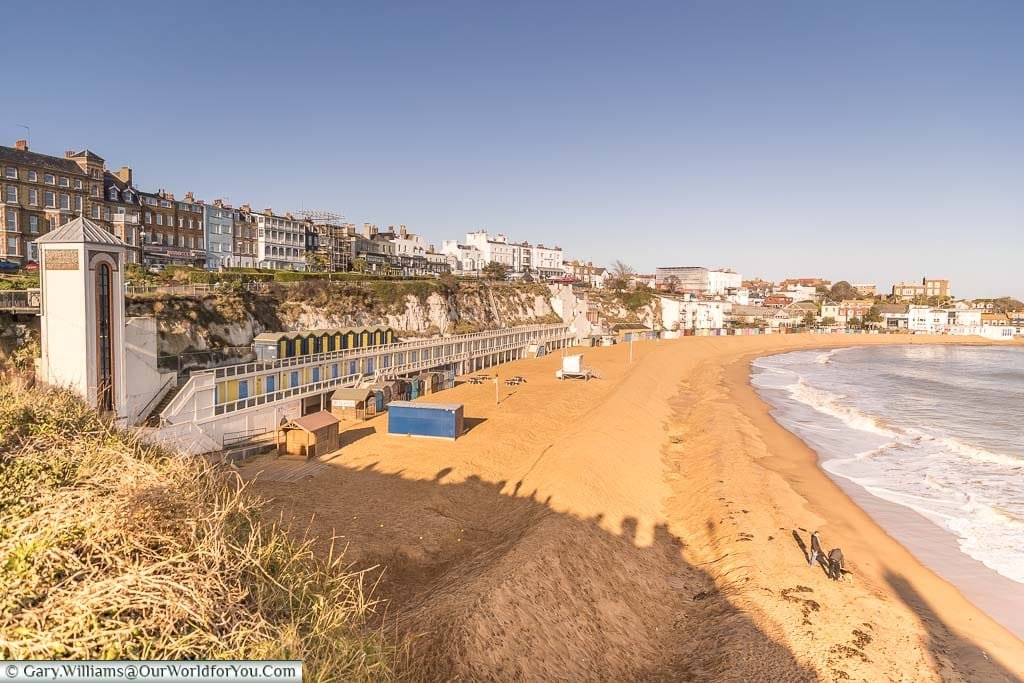 A view of Viking Bay as it sweeps around towards the harbour. On the left hand side you can see the lift What takes you to and from the promenade. also stretched out along the sea front you can see the bathing cabins.