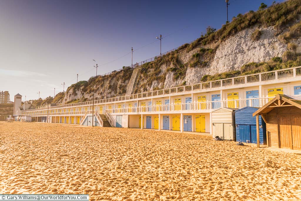 At the edge of the sands of Viking Bay is a row of beach cabins built into the cliff face. The doors of the cabins alternate between Bright yellow and a French blue
