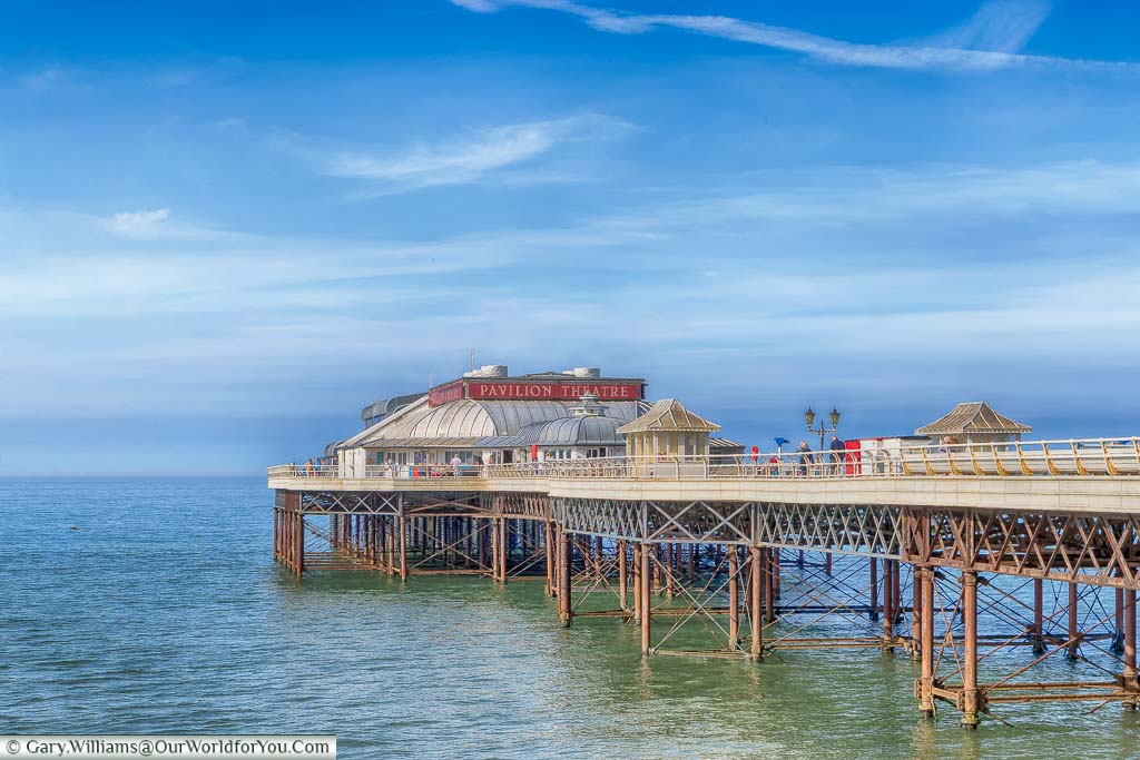 An off-centre view of Cromer Pier from the coastal path on a beautiful sunny day with blue skies. You can clearly see the wrought-iron framework and the Pavillion Theatre at the end