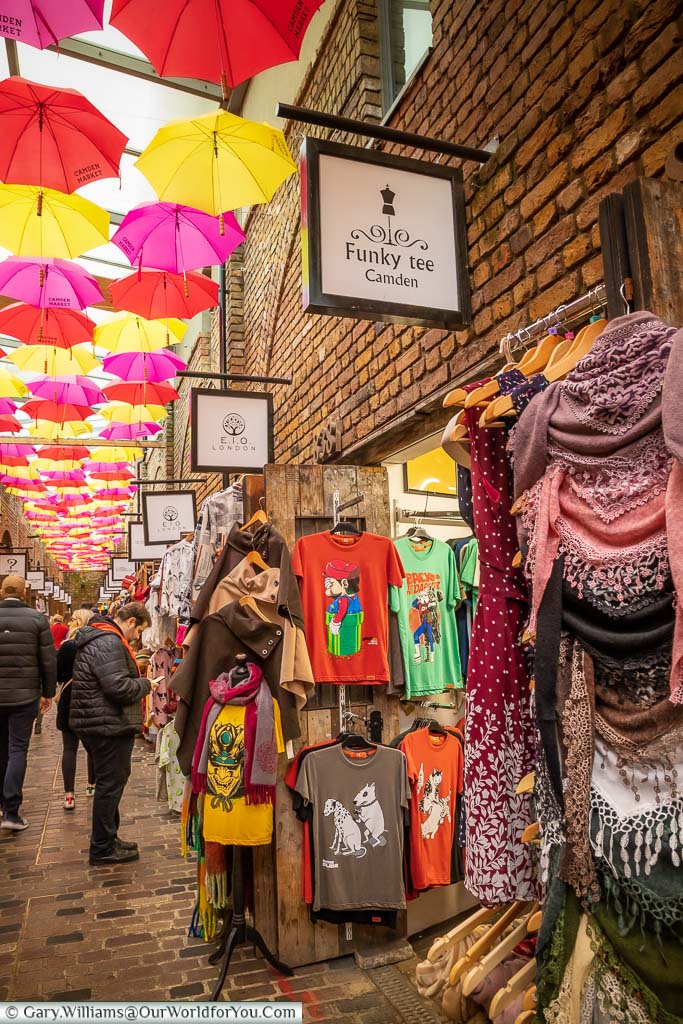 A mixture of pink, yellow &ed opened umbrellas provide a canopy over stores in one of the lanes in Camden Market