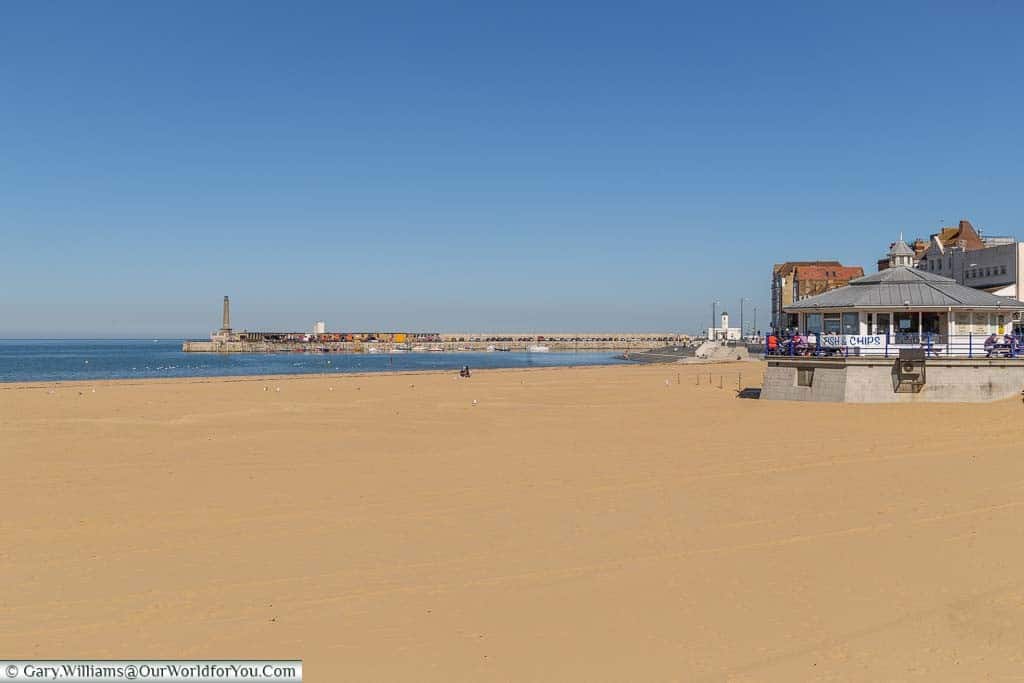 The golden sand of Margate's main beach, with a fish 'n' chip shop in the foreground. Margate's harbour arm can be seen in the distance.