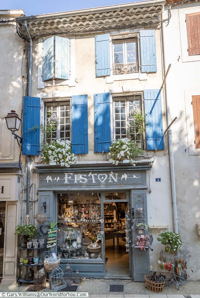 The front of a small Provencal gift shop with blue shutters over the window of the upper two storeys in St Remy de Provence.