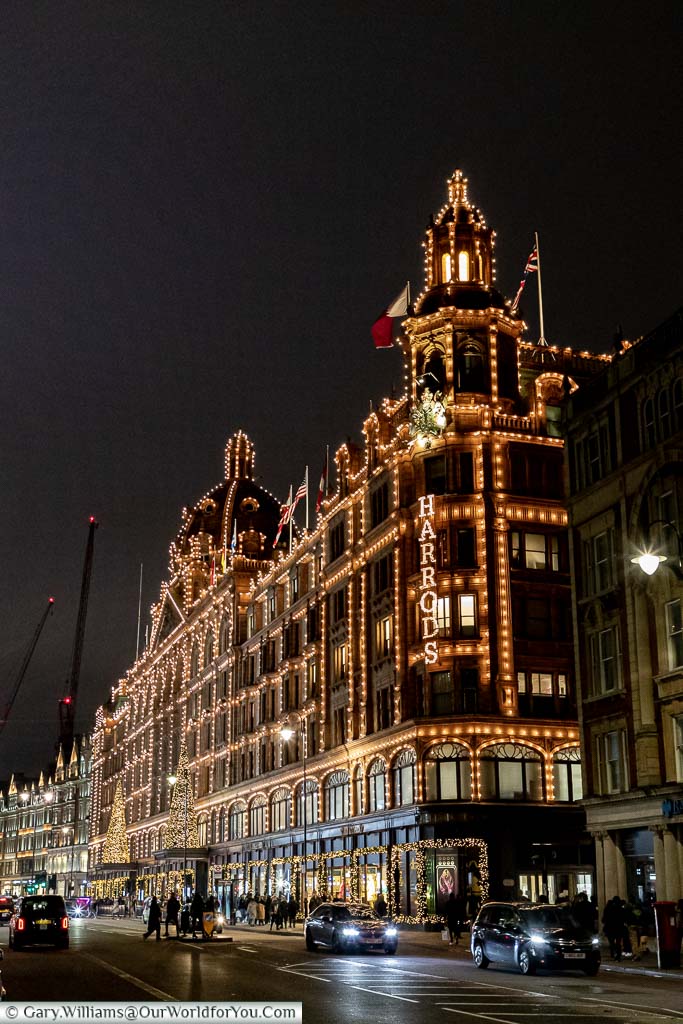 A view of the Harrods Department store in the evening decorated with hundreds of small lights and a pair of Christmas trees above the main entrance.