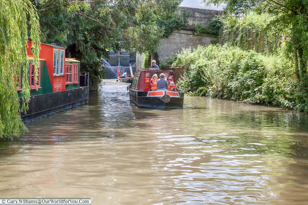 A narrow beam canal boat is exiting a lock with the children wearing life vests as a safety precaution.