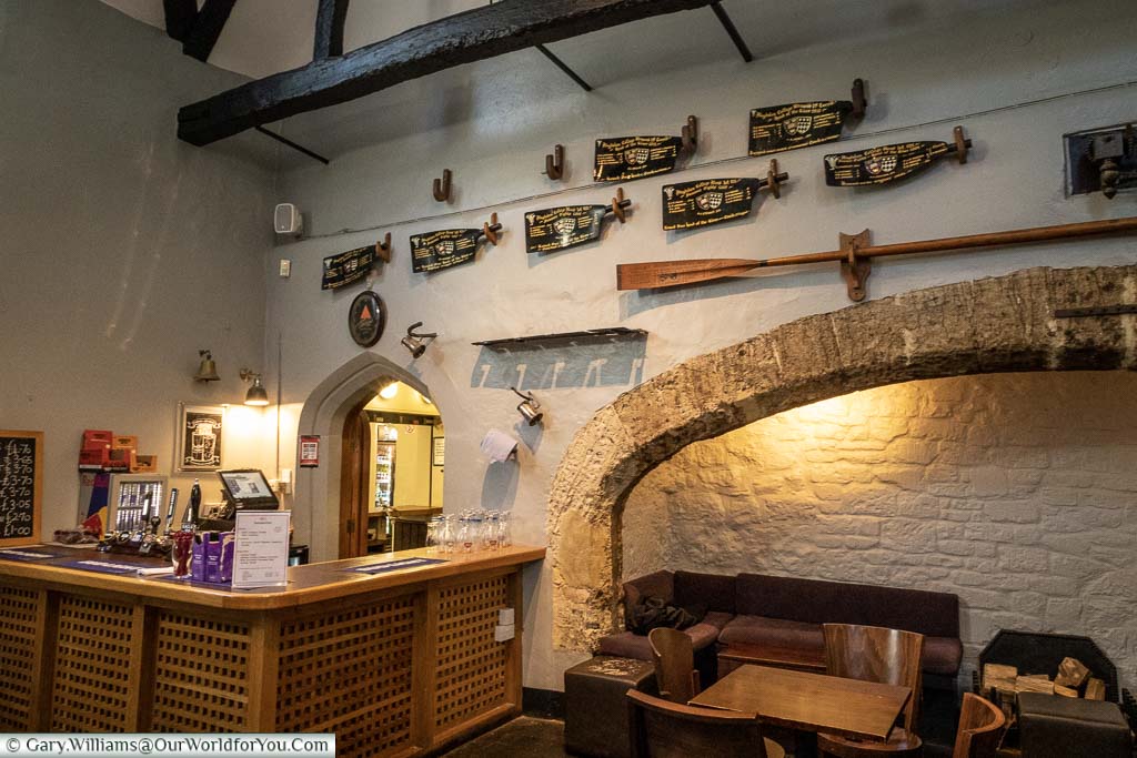 The Old Kitchen Bar of Magdalen College with an oar over the giant fireplace and commemorative oar blades decorating the wall.