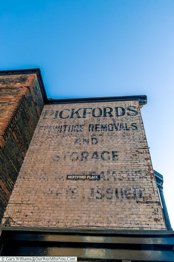 A painted shop sign on the edge of a brick building for Pickfords furniture removals and storage.