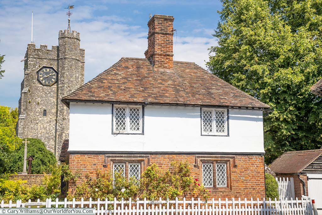 A pretty little house behind a white picket fence, with Chilham's church clock tower in the background.