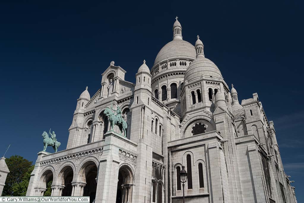 The white stone of the Sacré-Cœur Basilica in Paris set against a deep blue sky.