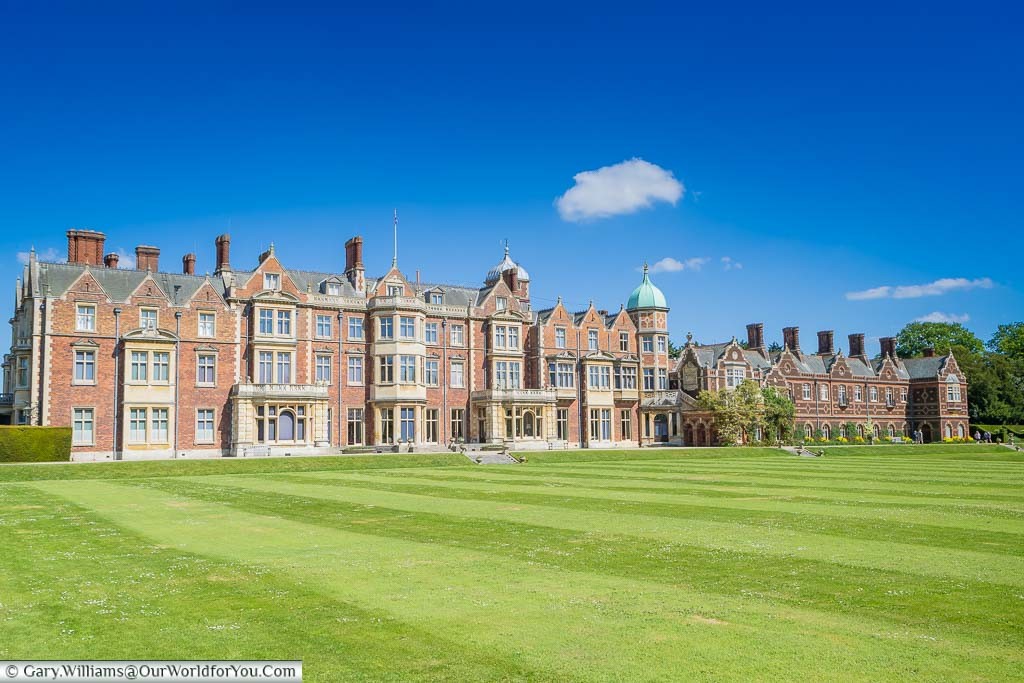The rear of Sandringham House across the well-manicured lawns, under blue skies, on a beautiful day in Norfolk.