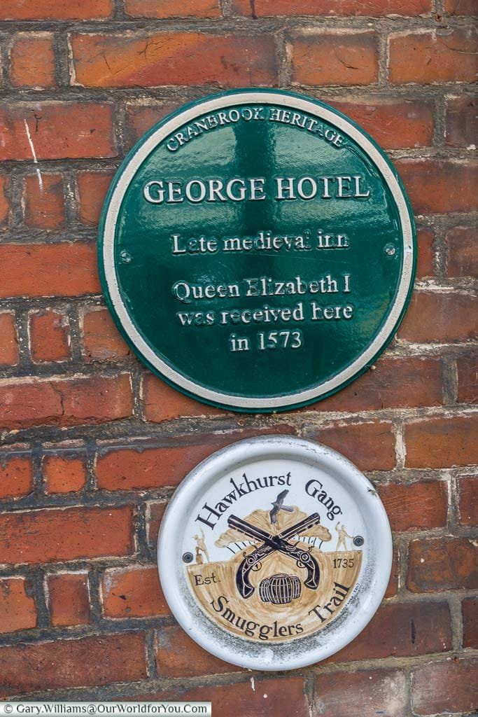 A green plaque from the Cranbrook Heritage society recognising the George hotel as a late medieval inn where Queen Elizabeth the 1st was received in 1573. A further plaque denotes the Hawkhurst Gang smuggler's trail.