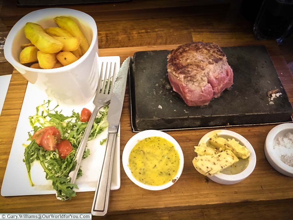 Steak cooking on a slab of volcanic rock at our table served with a pot of chips, a salad & accompaniments