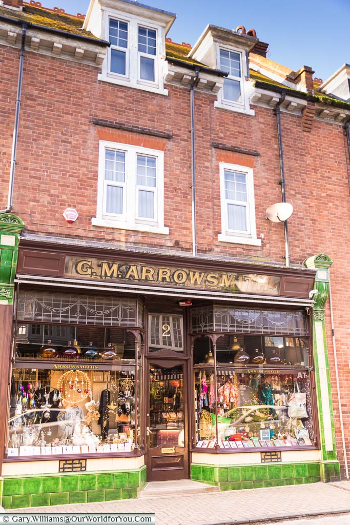 An ornate shop front in Broadstairs town, edged with green tiles and wooden bay windows, G.M. Arrowsmiths appears things to sell all manner of curious goods