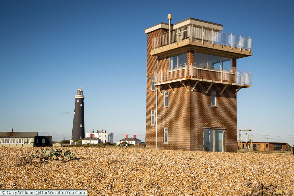 A view of the former brick-built, 10-metre tall Coastguard's tower on the shale beach of Dungeness, with the old lighthouse in the background.