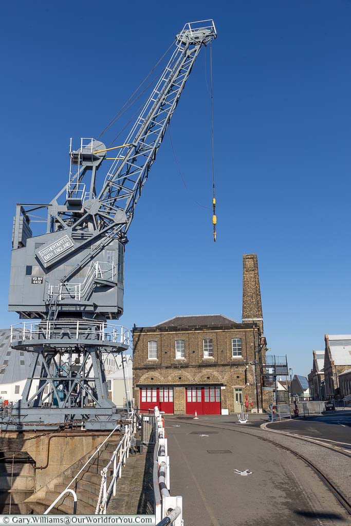 A grey dock crane in the foreground, and the brick-built fire station in the background, at the Historic Dockyard Chatham, Kent