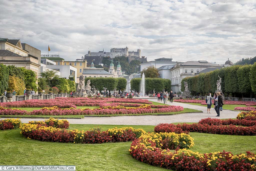 The Mirabell Palace Gardens in Salzburg with brightly coloured flower beds and fountain. In the distance, high on the hill, you can see the city's Castle.