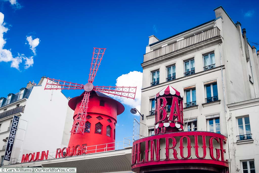 The roofline of the Moulin Rouge focusing on the bright red mill that takes centre stage set against a deep blue sky