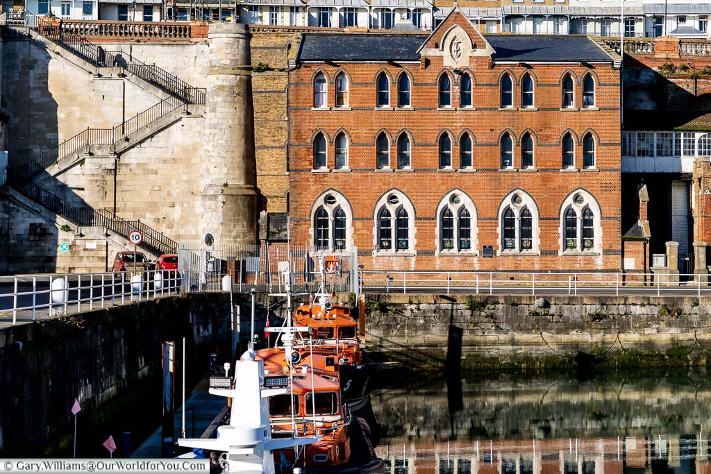 The red brick Sailors Church & Mission at the harbours edge. In the Harbour you can see pair of lifeboats moored up, ready for action