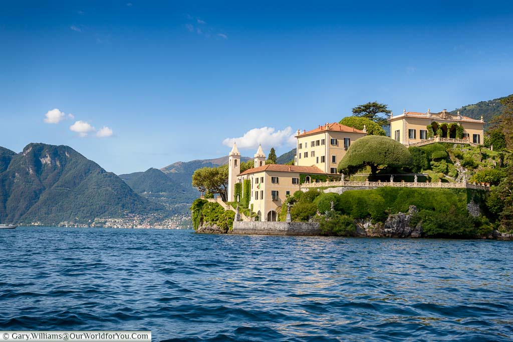 The palatial style Villa del Balbianello in sandy ones with terracotta tiled roofs against the backdrop of the deep blue water and blue skies of Lake Como