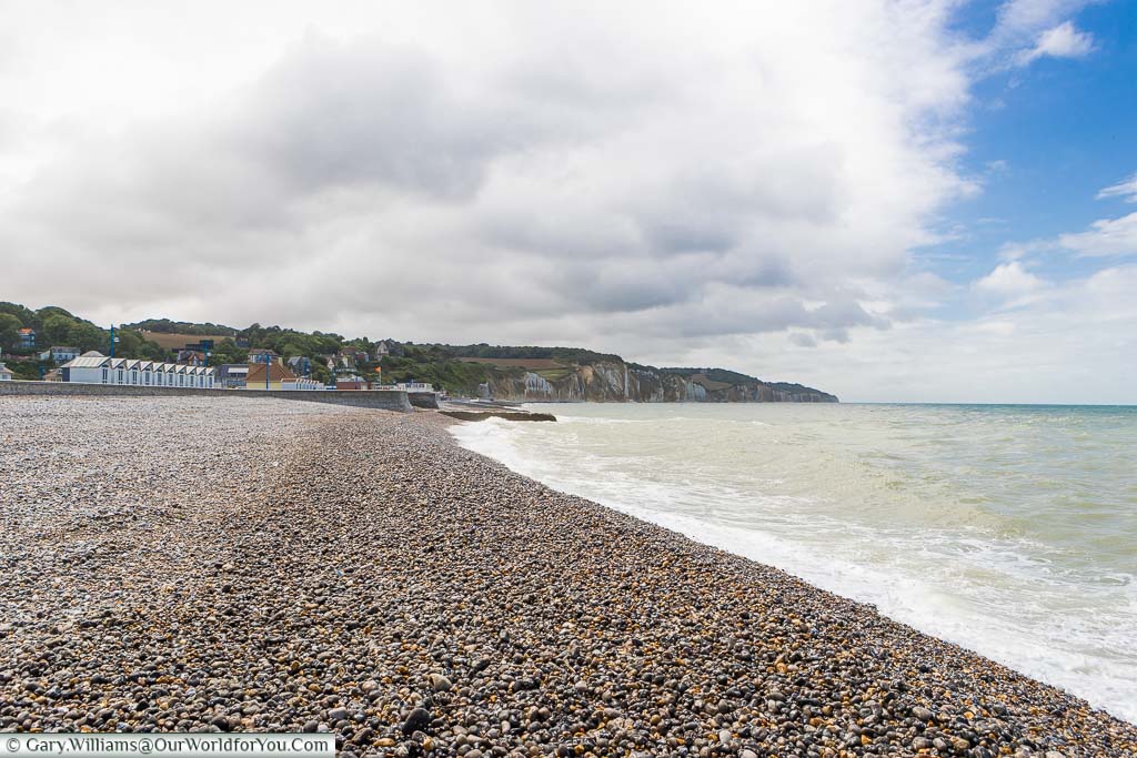 The Atlantic Ocean lapping against the shale beach at Hautot-sur-Mer with white chalk cliffs in the background.
