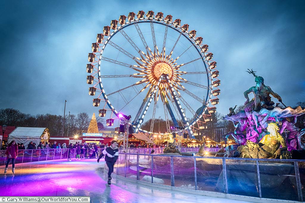 A skater on the ice rink around the Neptune fountain in Berlin, with the giant Ferris wheel in the background.