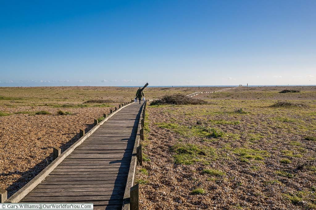 A lone fisherman walks along a wooden path over the shale beach at Dungeness.