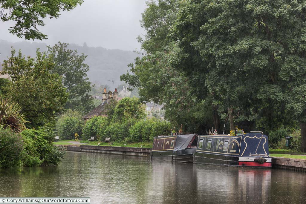 Narrowboats moored up alongside a towpath as the rain sets in. One of the perils of barging in the UK, even in summer.