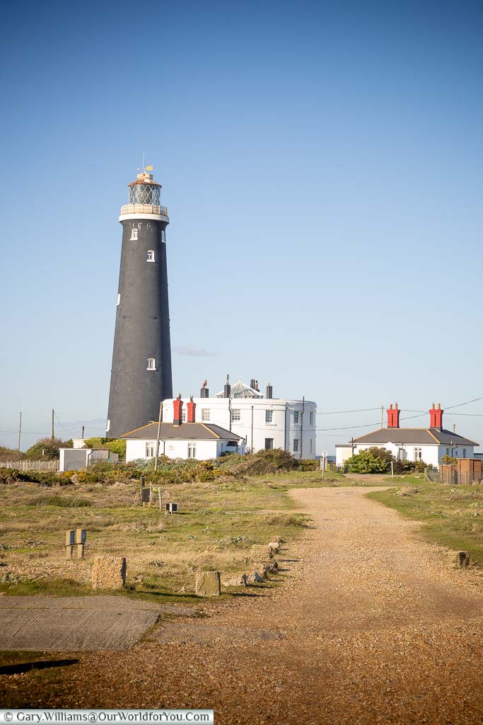 The black tower of Dungeness's forth lighthouse, next to the remaining two-storey white base of the third lighthouse.