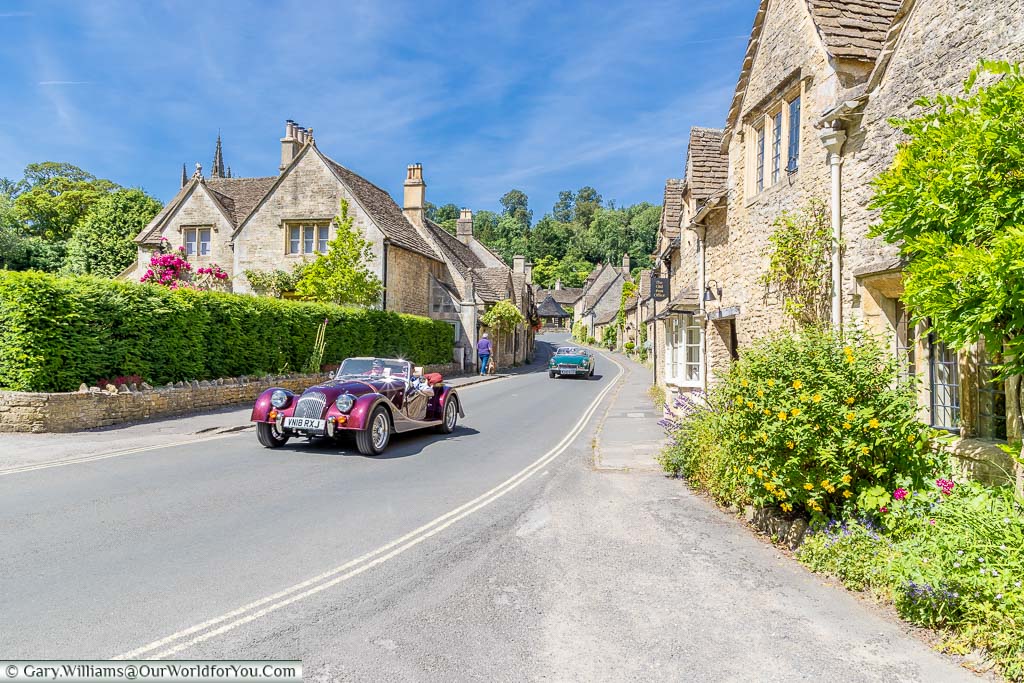 A classic Morgan sports car driving through the Cotswolds village of Castle Combe