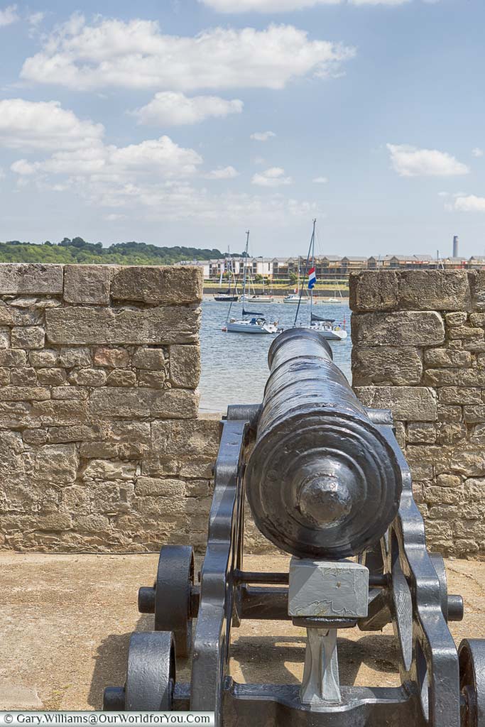 A cast-iron cannon, peering through a gap in a short stone wall to the River Medway beyond